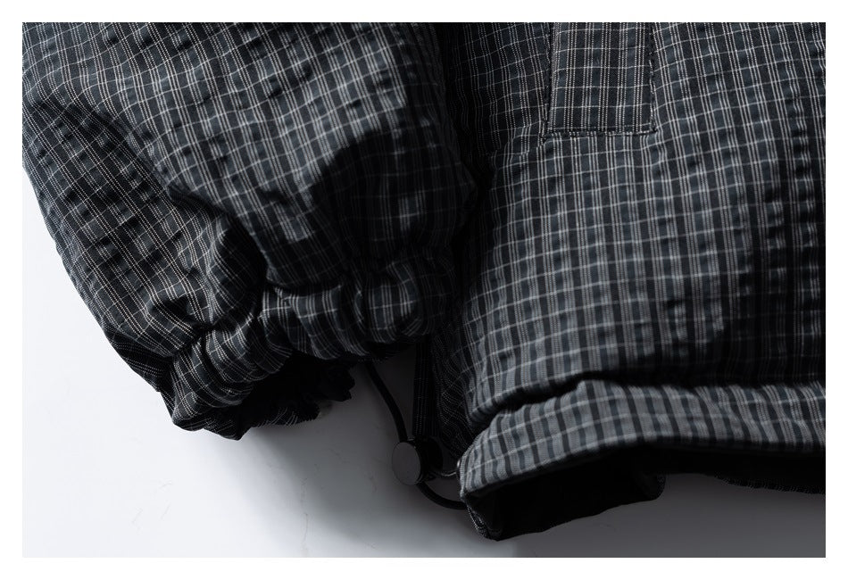 Close-up of a charcoal plaid garment showing a gathered sleeve cuff and cord toggle near the hem.