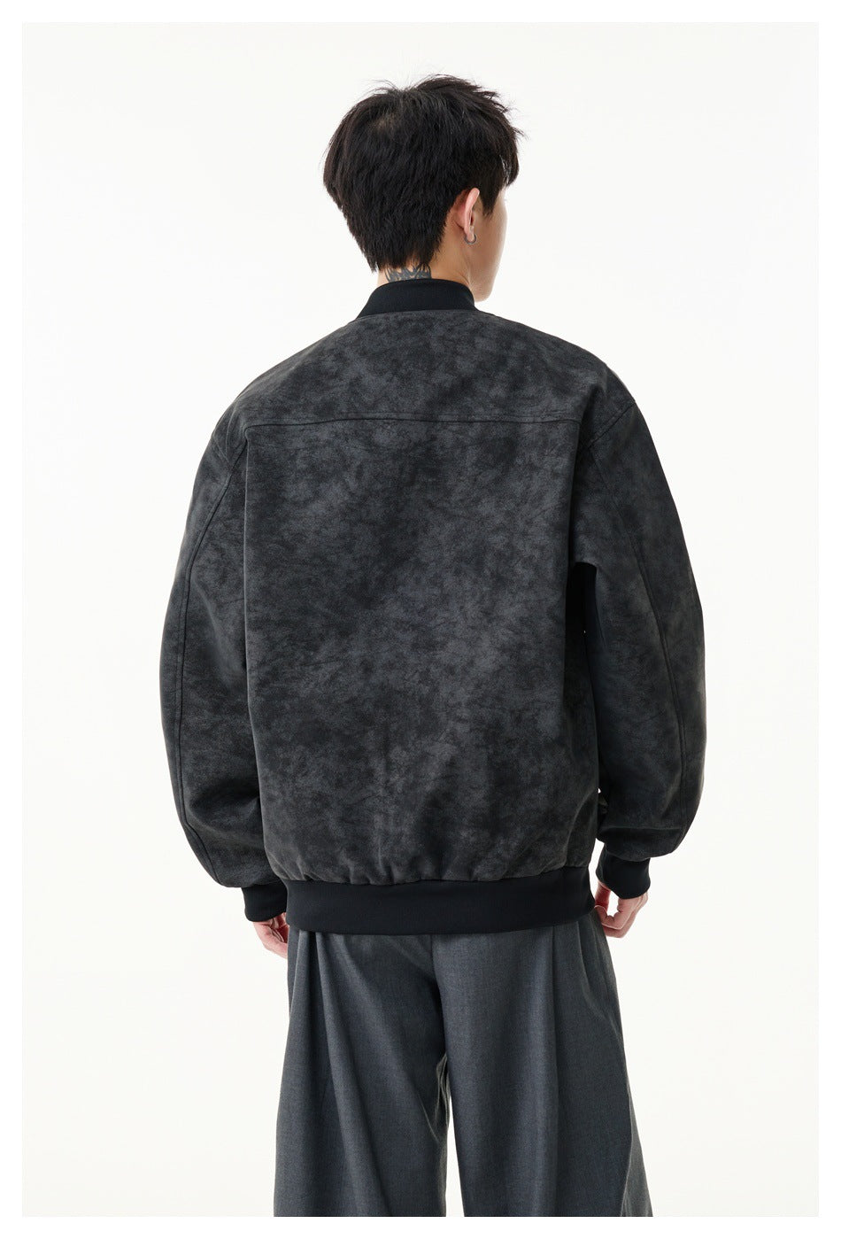Rear view of a model wearing a dark charcoal mottled jacket with a horizontal back yoke and ribbed hem.