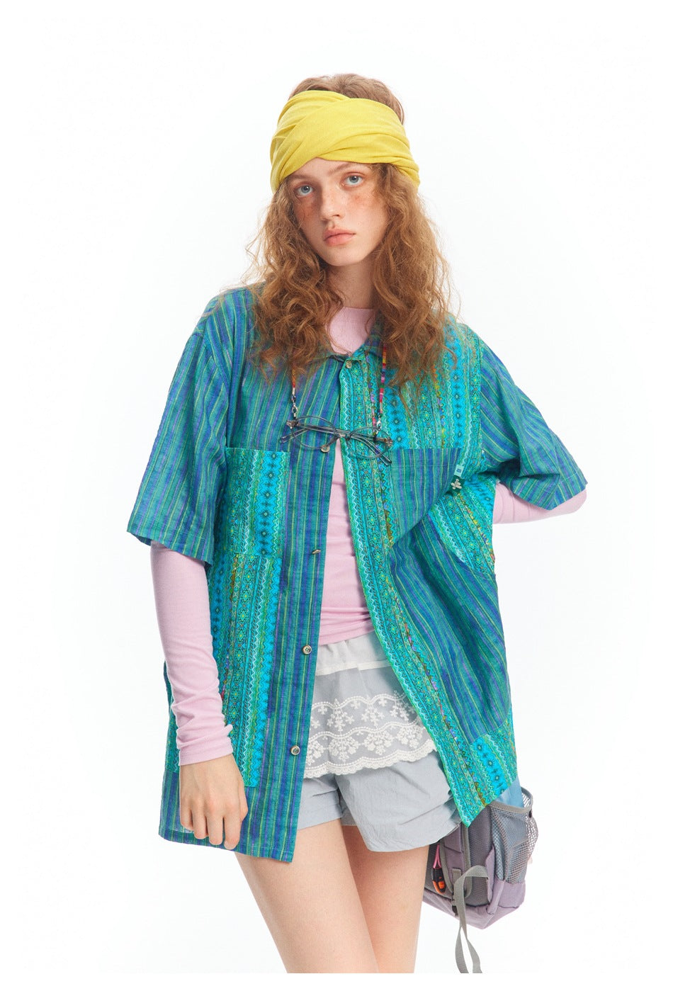 Model wearing a blue and turquoise patchwork-pattern short-sleeve tunic over a pink top and gray shorts.