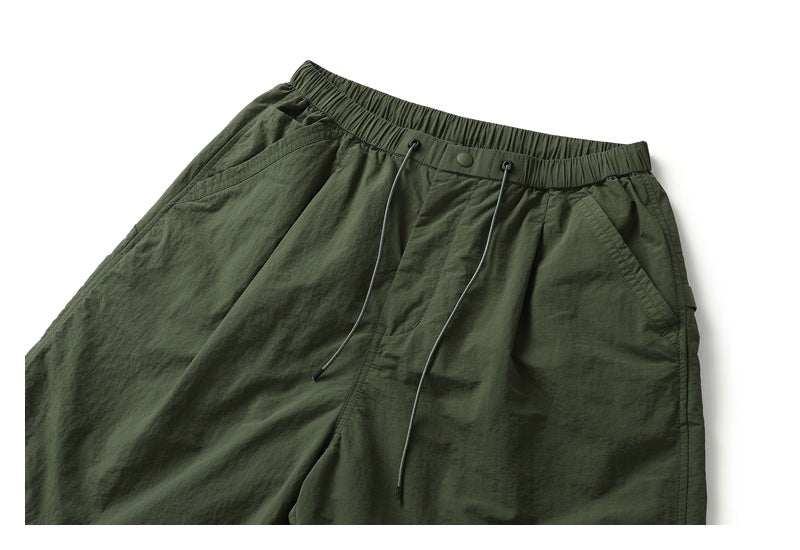 Close view of the front of dark olive shorts, showing the elastic waistband, long drawcords and angled side pockets.