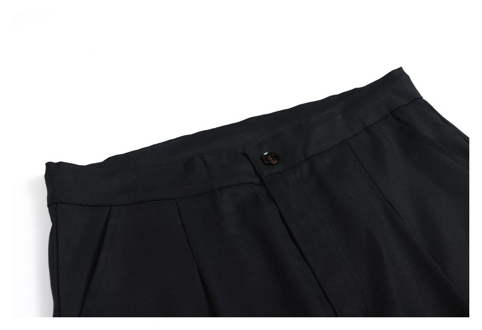 Close-up of black trousers showing the waistband, button, and front pleats.