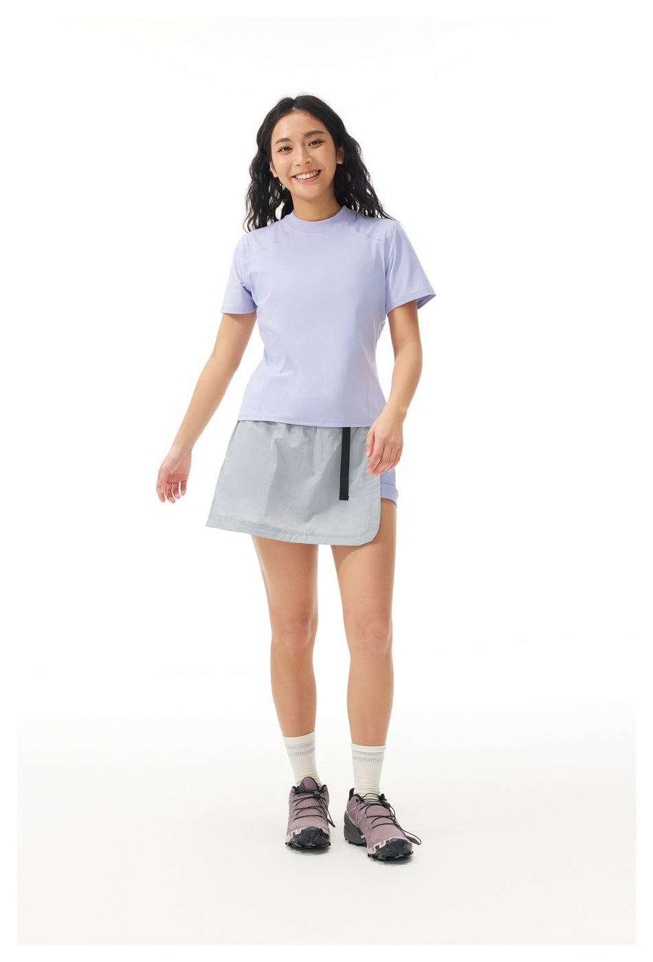 Model wearing a lavender short-sleeve T-shirt with a gray wrap-style tennis skirt over shorts.