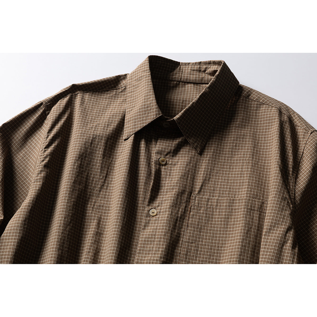 Close view of a brown plaid button-up shirt with a pointed collar and chest pocket.