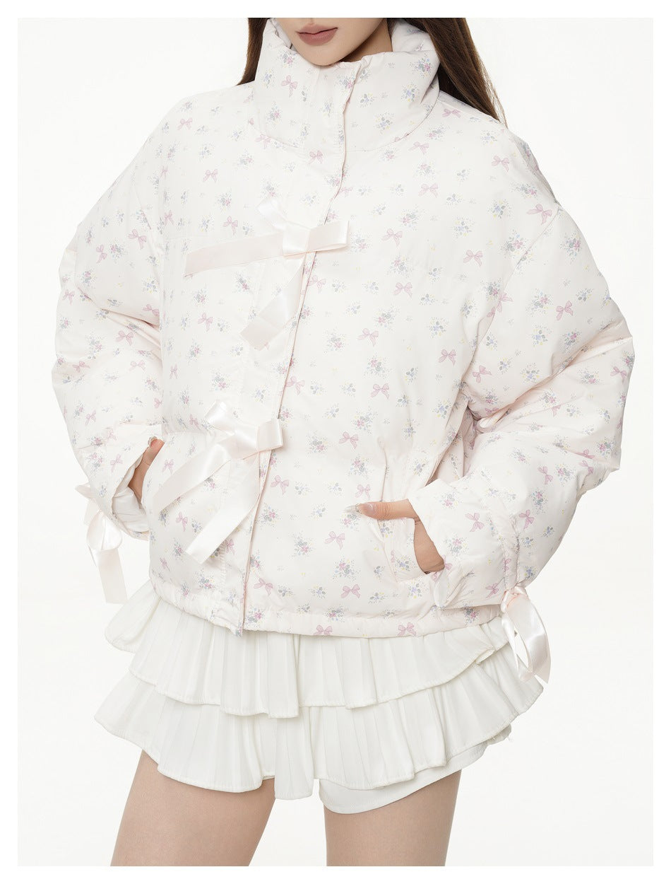 Close front view of a white jacket with a pastel bow-and-floral print, high collar, satin ribbon closures, and roomy sleeves.