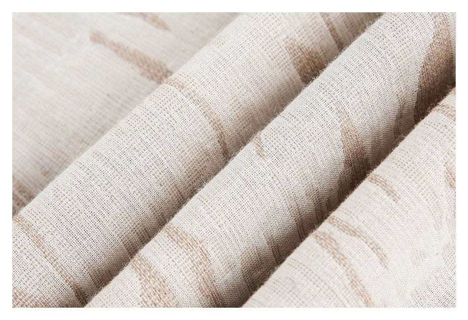 Close-up of pale cream fabric folded into soft ridges, showing a woven texture and tan abstract pattern.