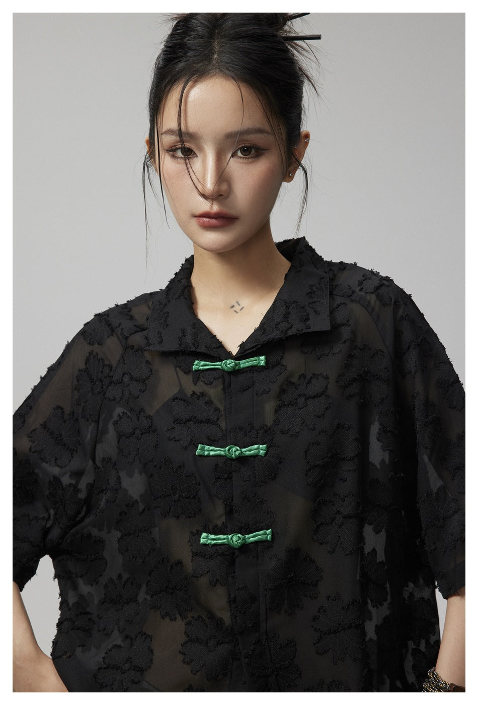 Model wearing a black sheer floral shirt with a pointed collar and green frog closures.