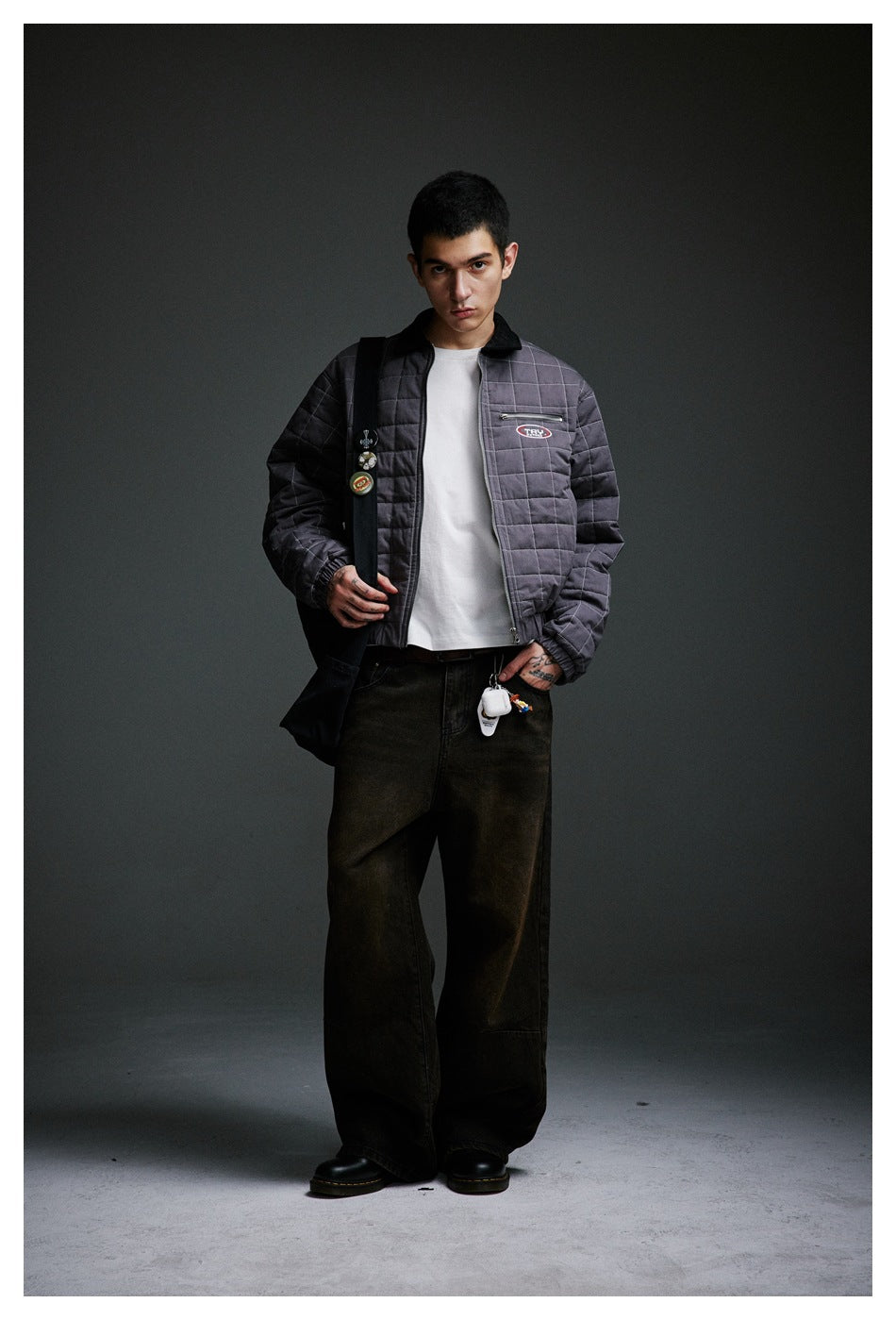 Front view of a model wearing an open charcoal-gray quilted jacket with a black collar and chest zip pocket.