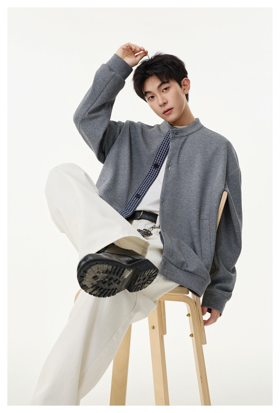 Model seated on a wooden stool wearing a gray stand-collar jacket with gingham placket, white tee and cream wide pants