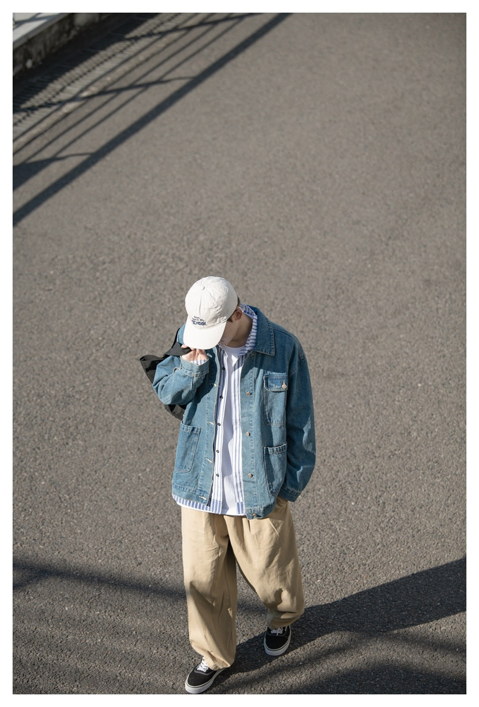 Model in a blue denim jacket and tan trousers, viewed from above while walking outdoors.