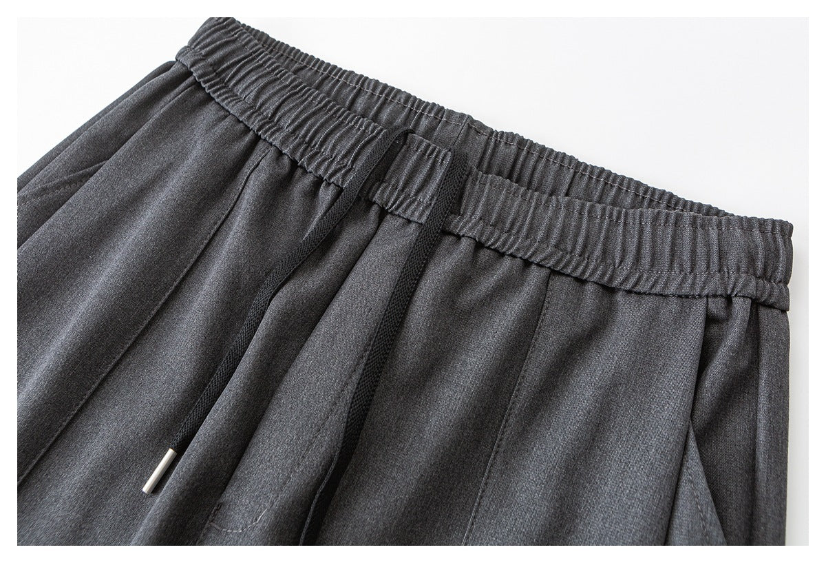 Close-up of charcoal gray pants with a gathered elastic waistband, front pleats and a drawcord with a metal tip.