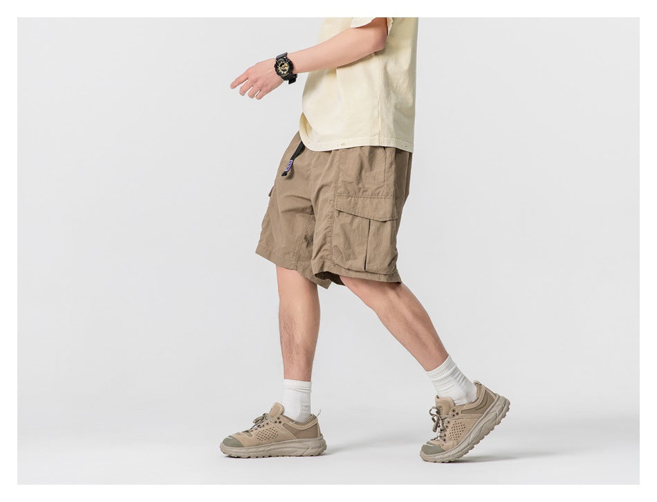 Model wearing tan cargo shorts with large flap pockets, shown from the side while walking.