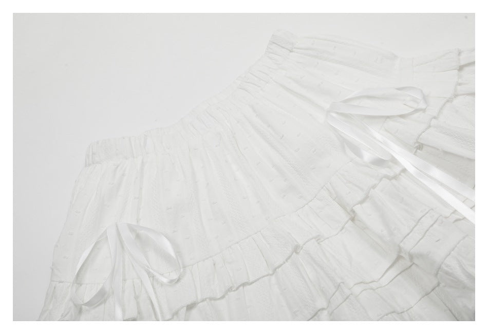 Angled close-up of a white skirt's gathered waist, textured panels, ruffles, and satin ties.