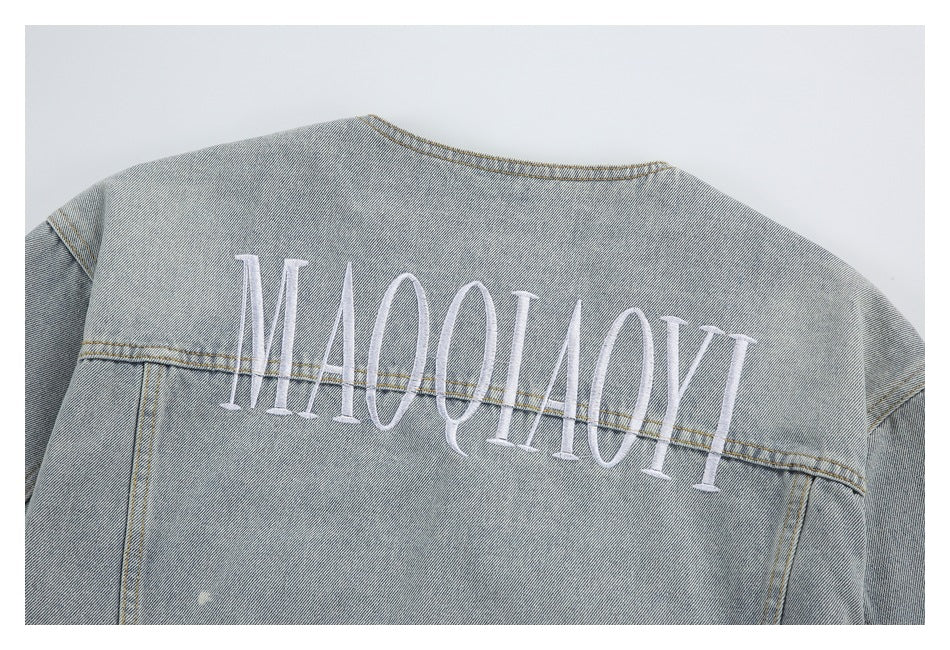 Back of a light blue acid-wash denim jacket with large white embroidered lettering across the shoulders.