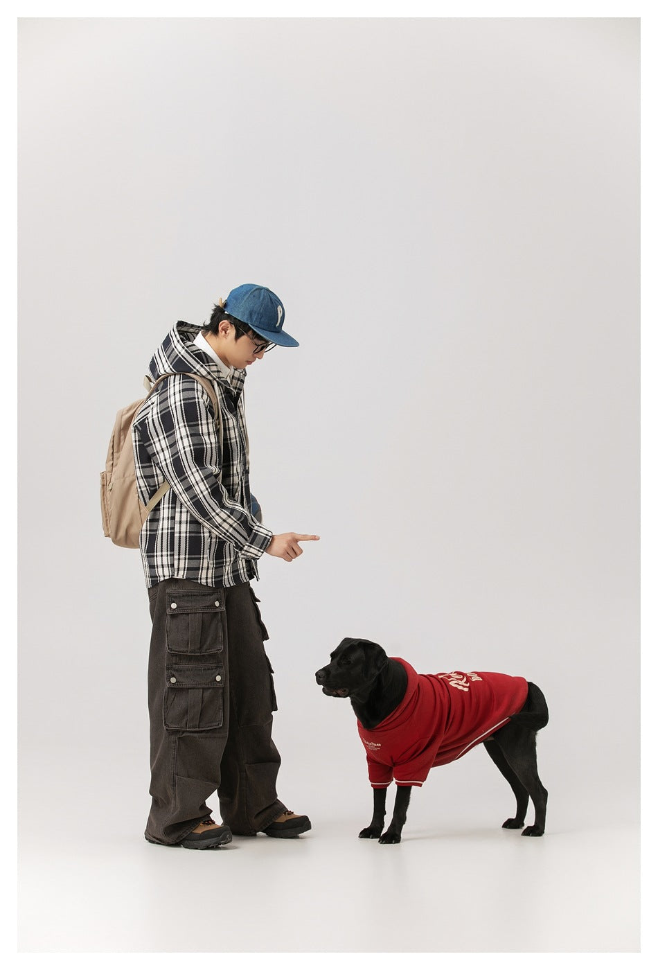Side view of a model in a black-and-white plaid hooded jacket beside a dog wearing a red shirt.