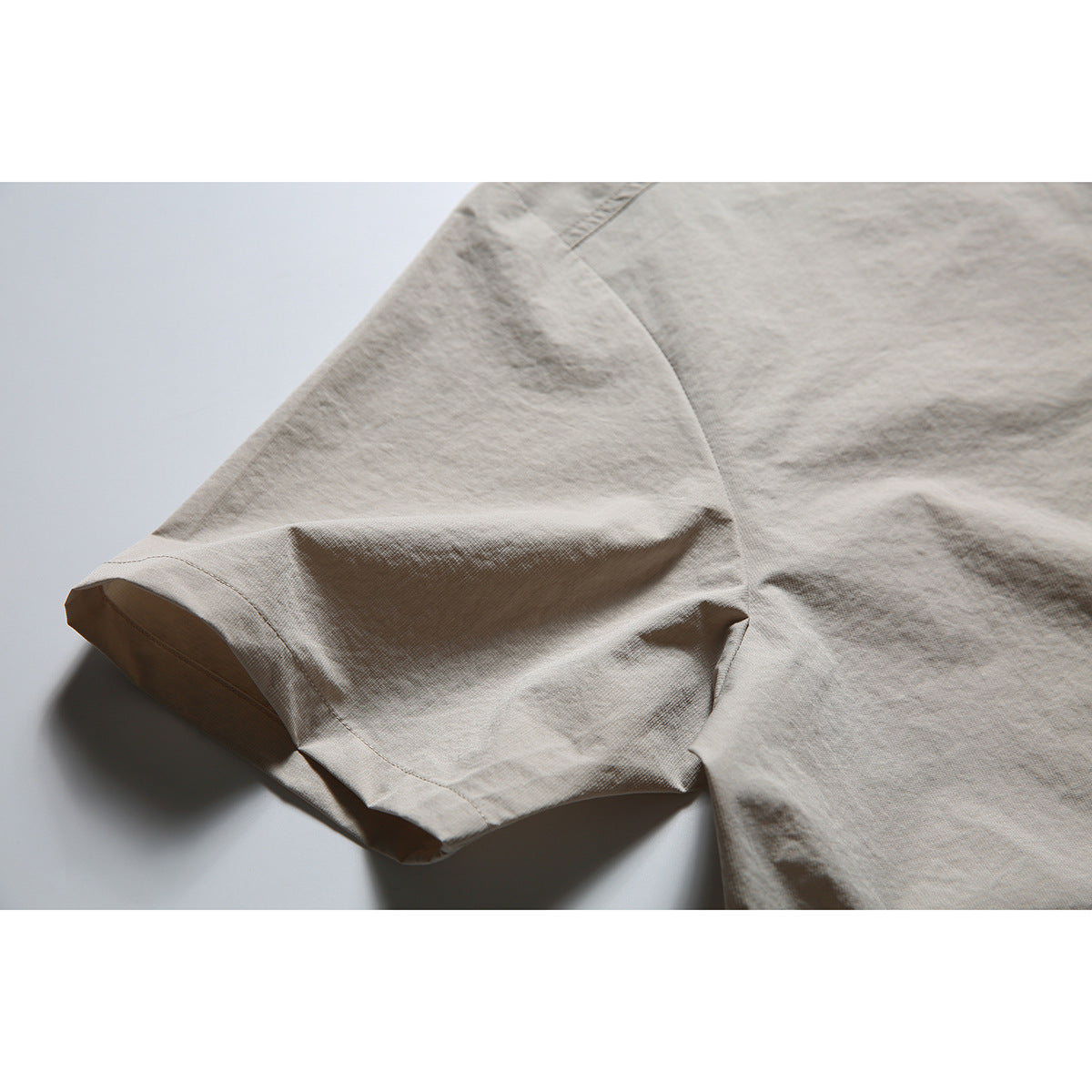Close-up of the taupe shirt's short sleeve, hem stitching and side seam.