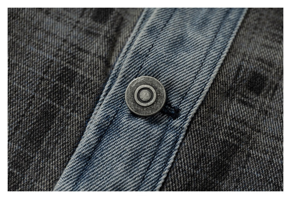 Close-up of a dark metal button on the light blue denim front placket against charcoal plaid fabric.