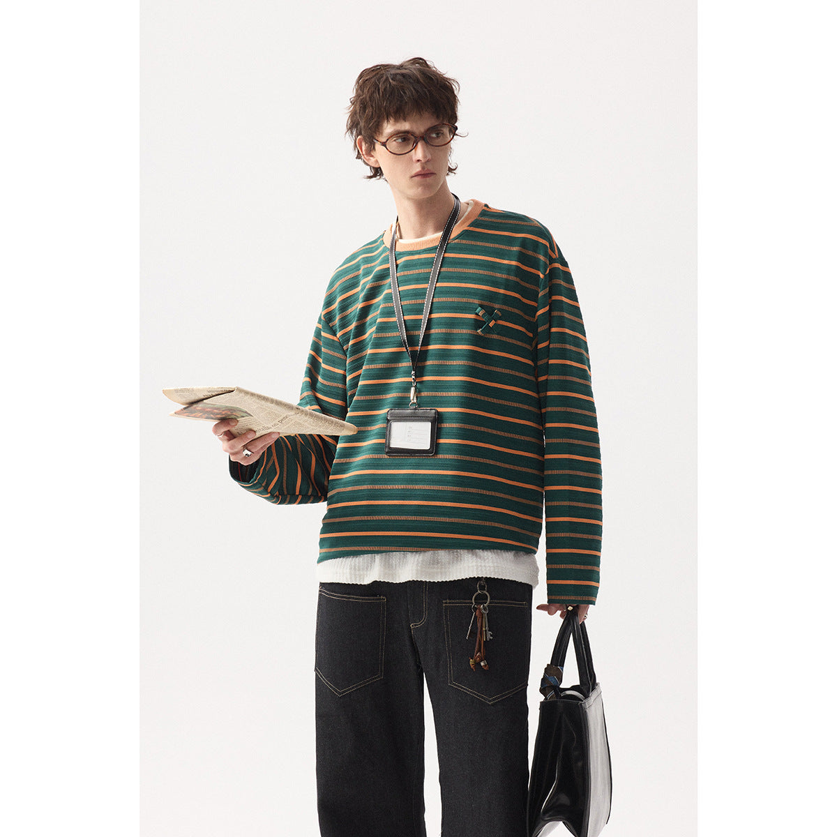Model wearing a loose dark green long-sleeve shirt with orange horizontal stripes and a small chest detail.
