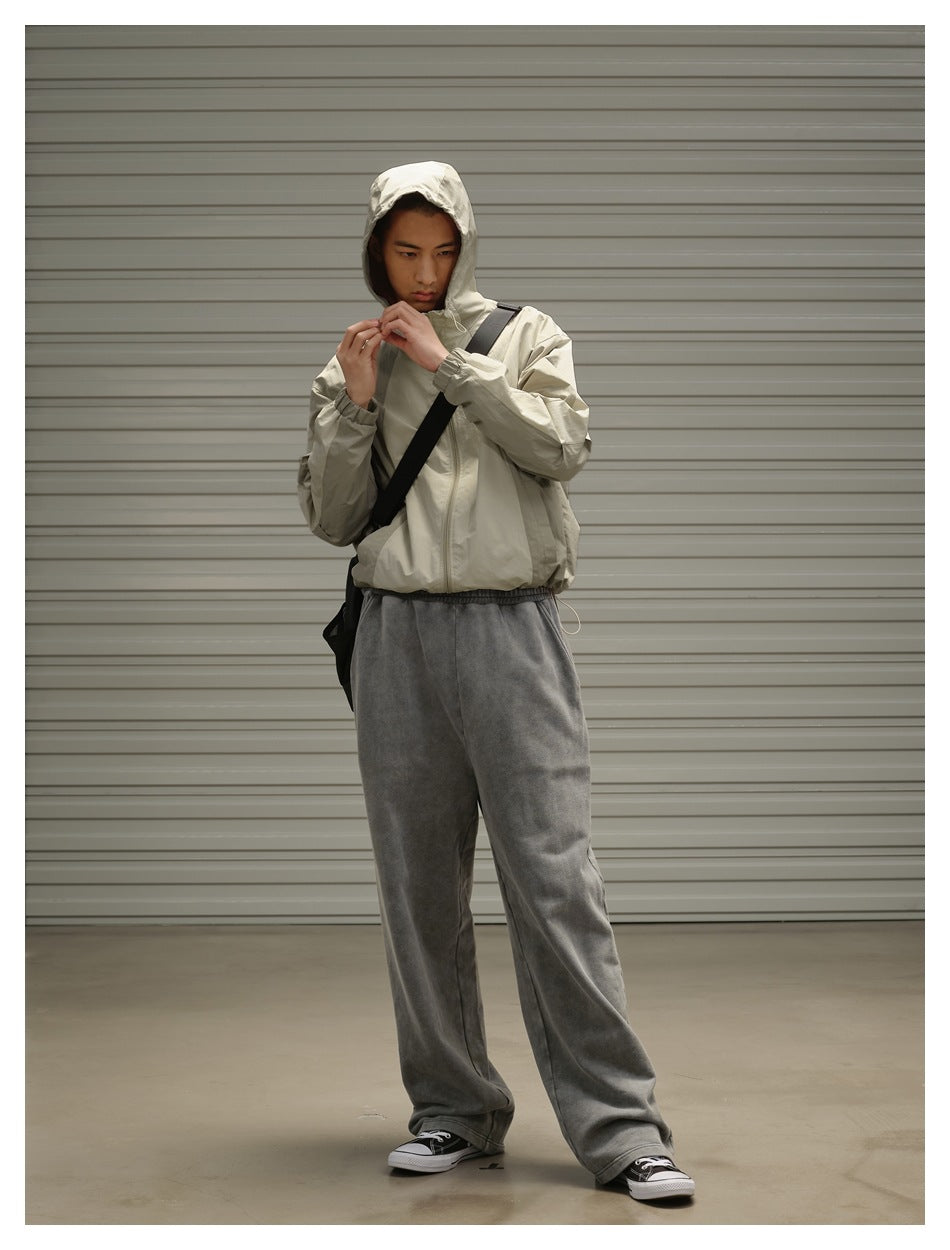 Model adjusting the hood of a light beige jacket, paired with loose charcoal gray pants and a black crossbody bag.