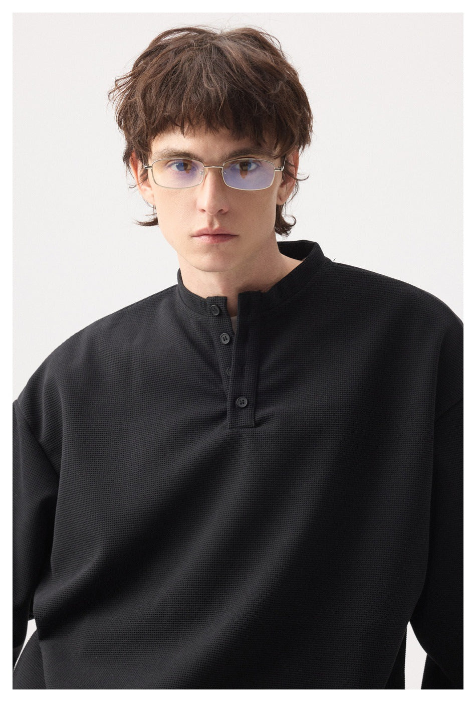 Model wearing a black textured long-sleeve henley shirt with a short button placket and band collar.
