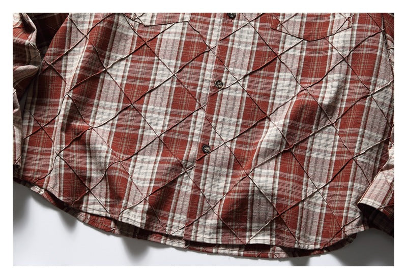 Close view of a red, cream, and gray plaid button-front shirt with layered diamond-shaped fabric panels.