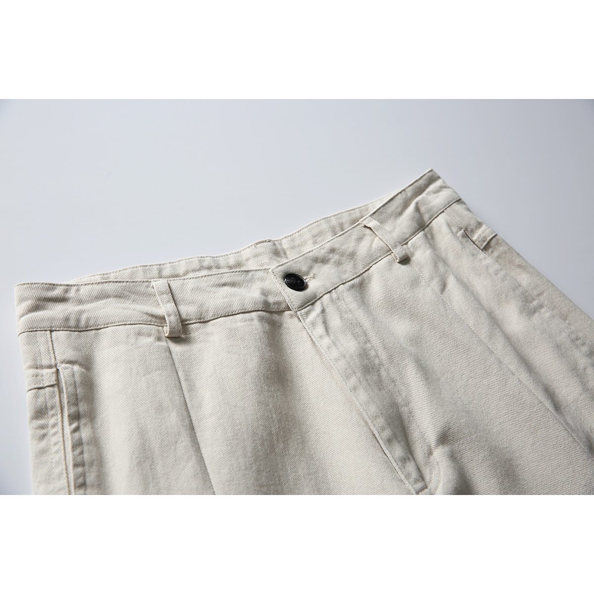 Close-up of light beige wide-leg trousers showing the waistband, belt loops, black button and front pleats.