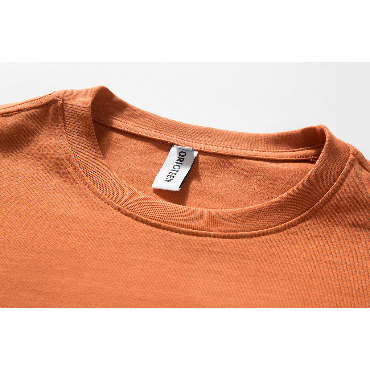 Close-up of the orange T-shirt's ribbed crew neck and inner ORIGTEEN label.
