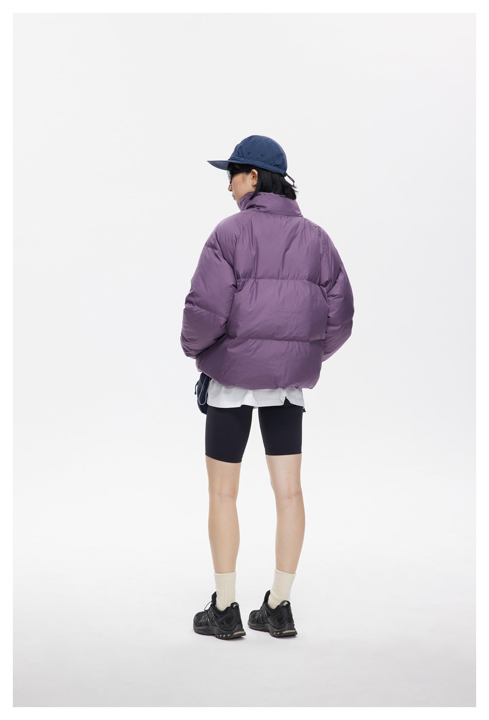 Rear view of a model wearing a plum-purple quilted puffer jacket with a high collar and roomy sleeves.