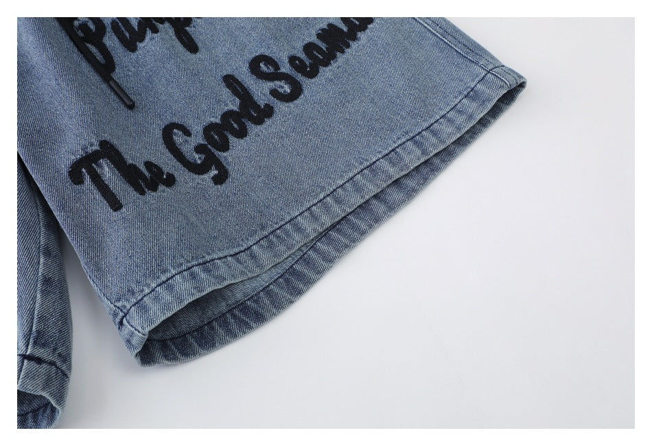 Close-up of the stitched hem and black script graphic on a blue denim shorts leg.
