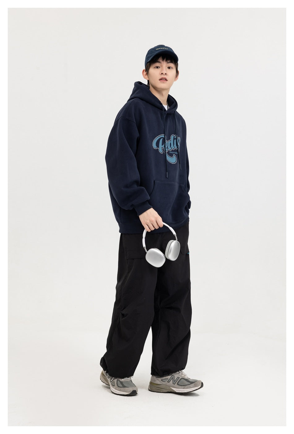 Model wearing a navy graphic hoodie, shown at a three-quarter angle while holding silver headphones.
