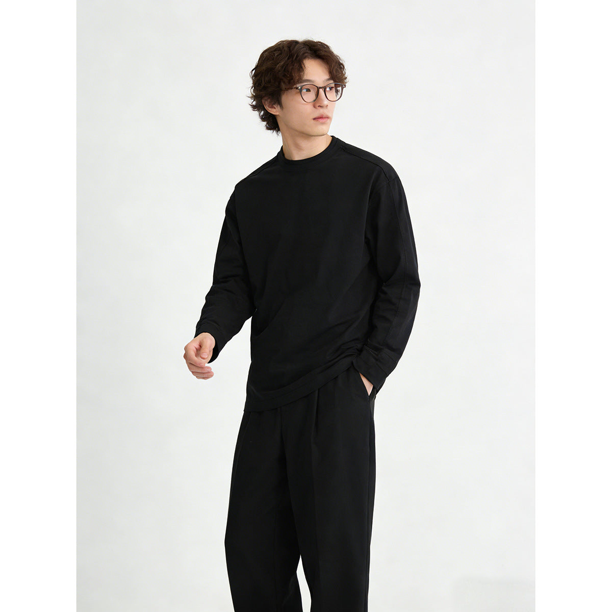 Model wearing a plain black crewneck sweatshirt and black trousers, shown at a three-quarter angle.