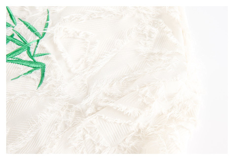 Close-up of ivory fabric with a fringed surface and partial green bamboo embroidery.