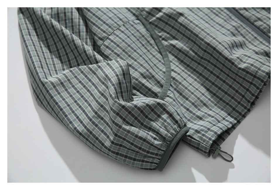 Close-up of the plaid jacket's gathered sleeve cuff, curved pocket opening, and adjustable hem toggle.