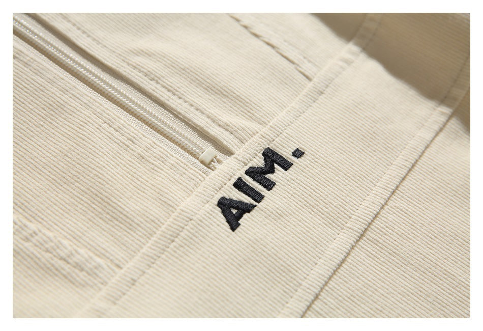 Close-up of a cream ribbed garment with a black embroidered AIMI logo beside a zipper.