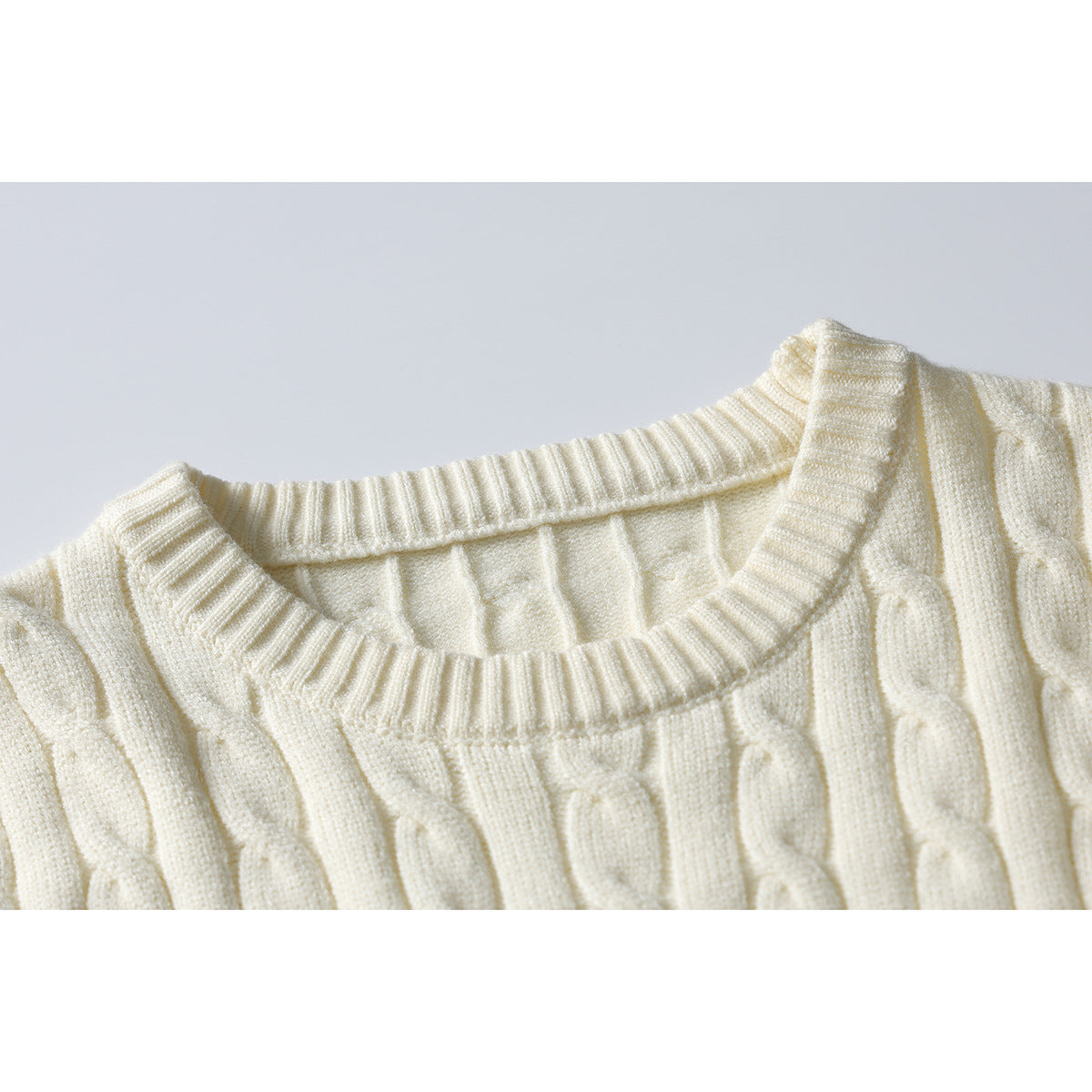 Close-up of an ivory cable-knit sweater showing its ribbed crew neckline and raised knit pattern.