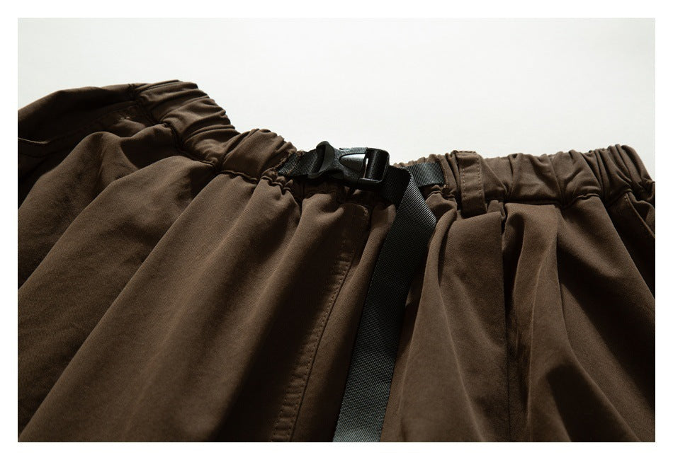 Close-up of dark brown trousers with an elastic waistband and black adjustable buckle belt.