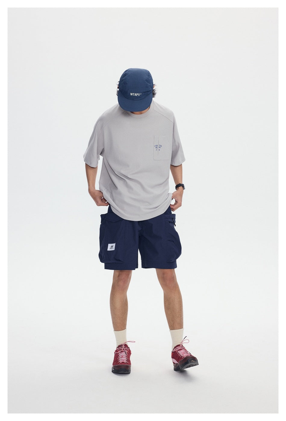 Front view of a model wearing a light gray pocket T-shirt, navy cargo shorts, and a navy cap.