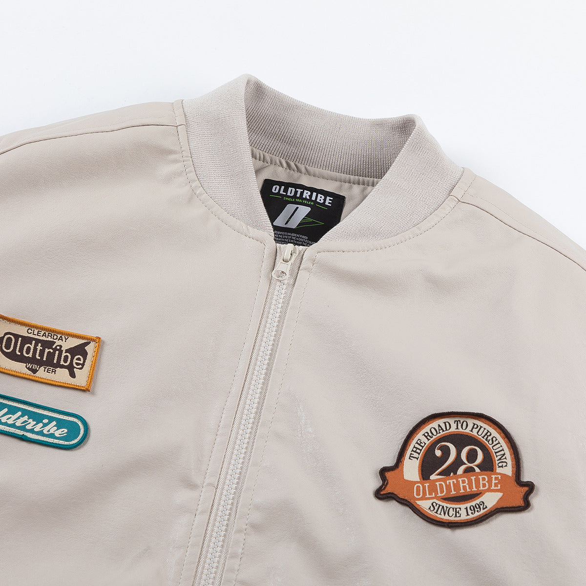 Close-up of an ivory bomber jacket's ribbed collar, front zipper, and embroidered chest patches.