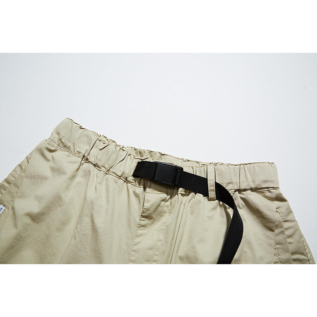 Close-up of beige shorts with an elastic waistband and black webbing belt and buckle.