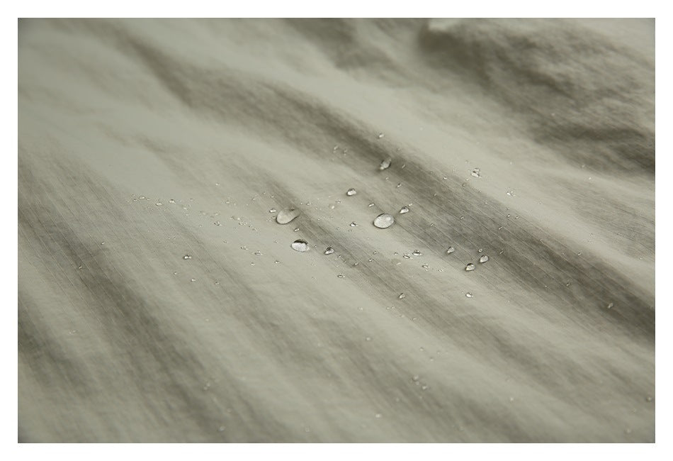 Water droplets bead on the gray-green jacket fabric.