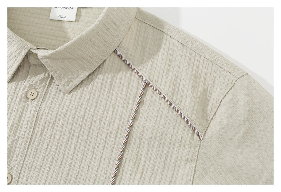 Close-up of a cream shirt collar and shoulder with striped piping and a visible neck label.