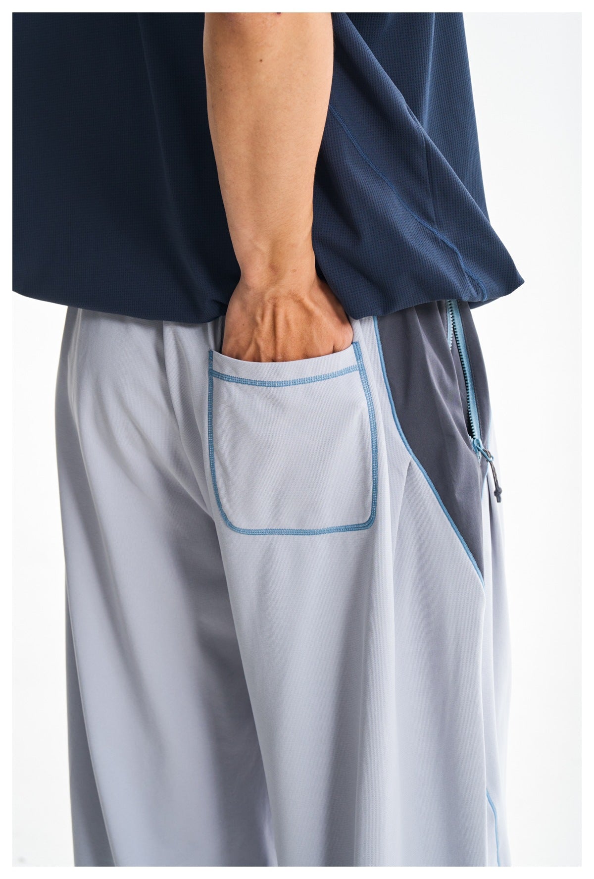Close-up of a light gray pants pocket with blue stitching and trim, shown beneath a navy shirt.