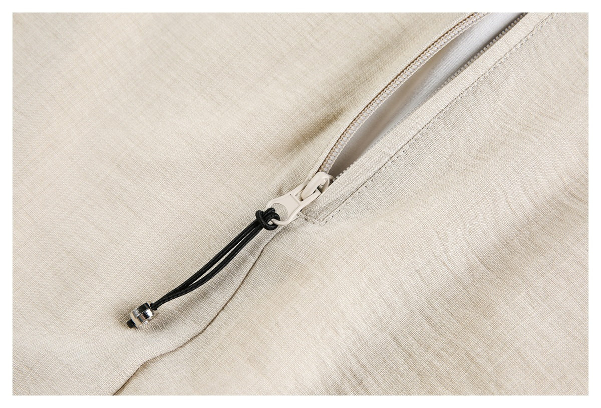 Close-up of an ivory garment's diagonal zipper pocket with a black cord pull and metal tip.