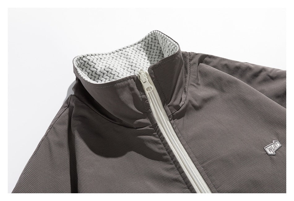 Close-up of a gray jacket's high collar, pale zipper, patterned inner lining, and small embroidered chest emblem.