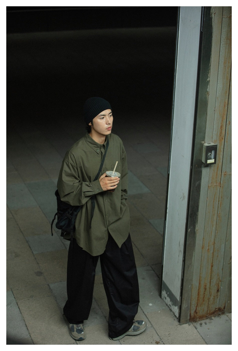 Full-length view of a model in an oversized olive-green shirt and wide black trousers.