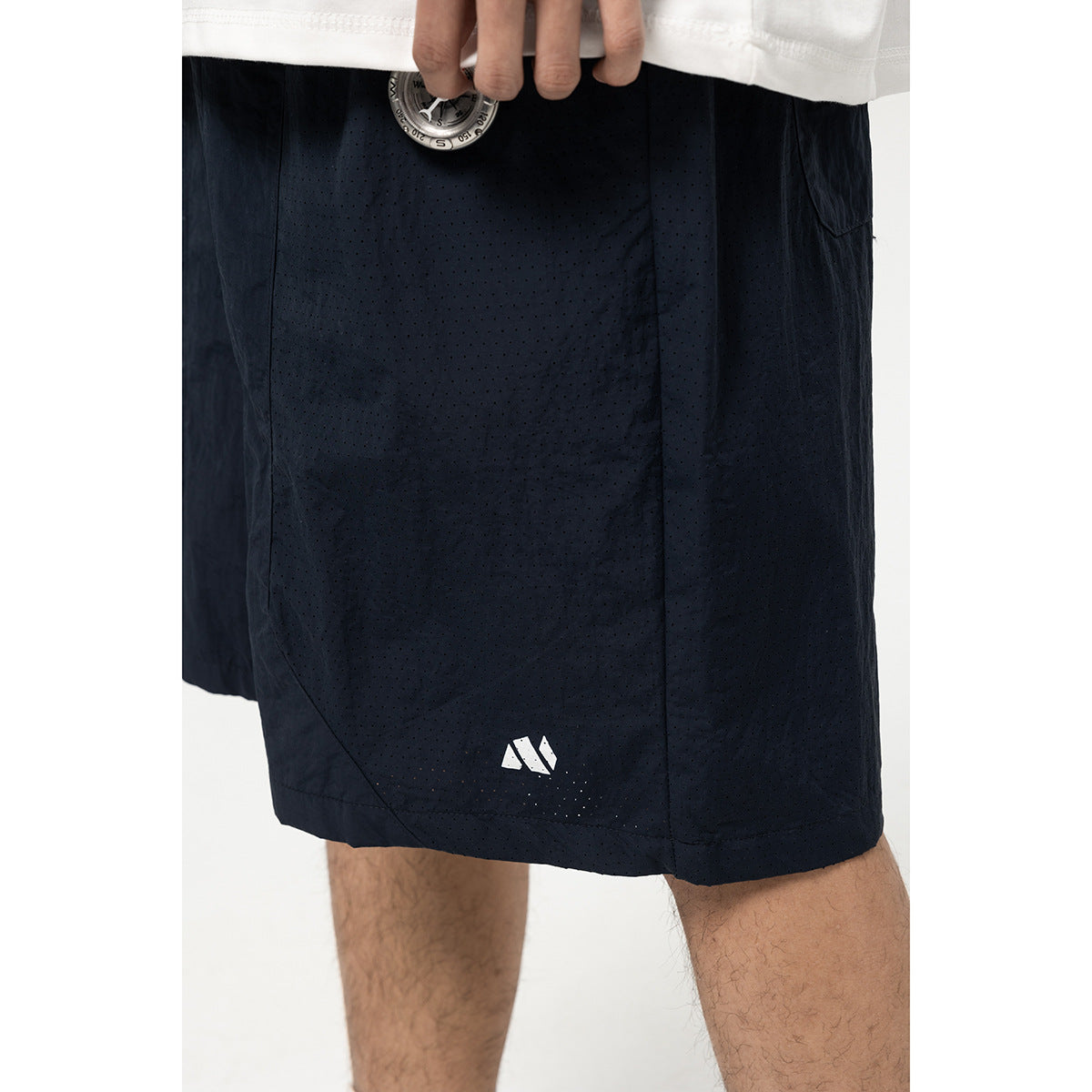 Close-up of dark navy perforated shorts with a small white geometric logo near the hem.