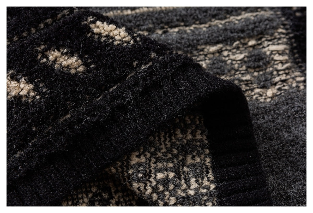 Close-up of black and charcoal patterned knit fabric with cream motifs and a dark ribbed edge.