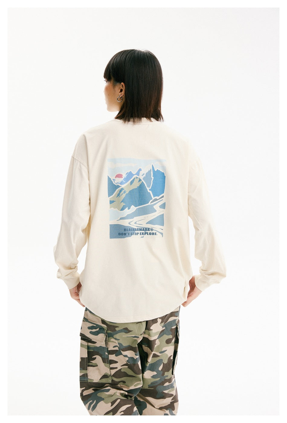 Closer rear view of an ivory long-sleeve shirt with a blue mountain graphic, worn with camouflage cargo pants.