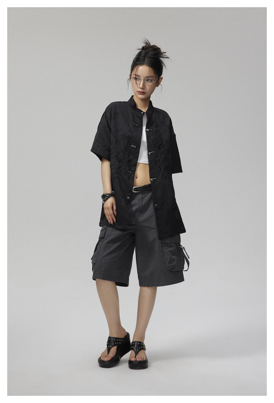 Model wearing a black oversized short-sleeve jacket with a stand collar, metal frog closures and botanical embroidery.