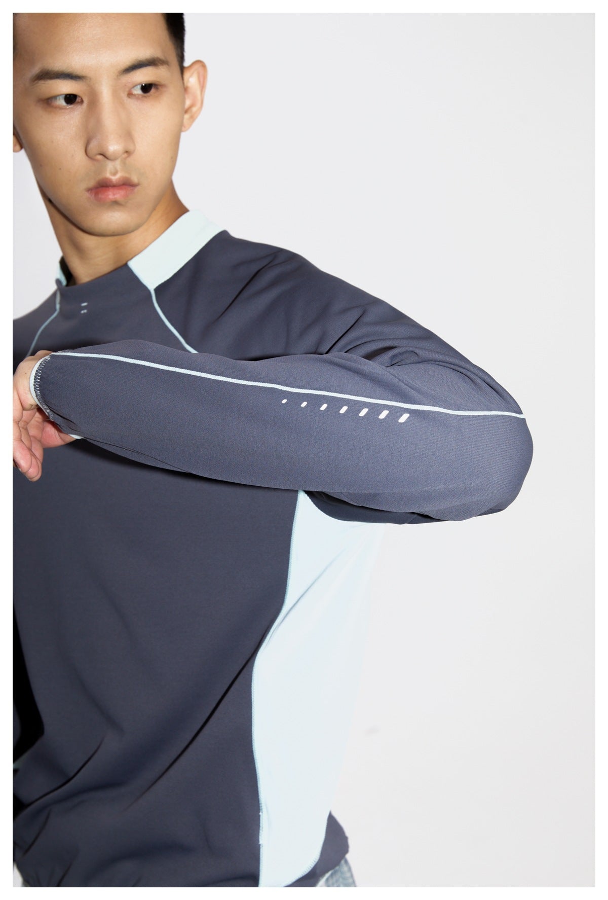 Model wearing a charcoal top with pale aqua side panels, raising an arm to show the sleeve's piping and dash details.