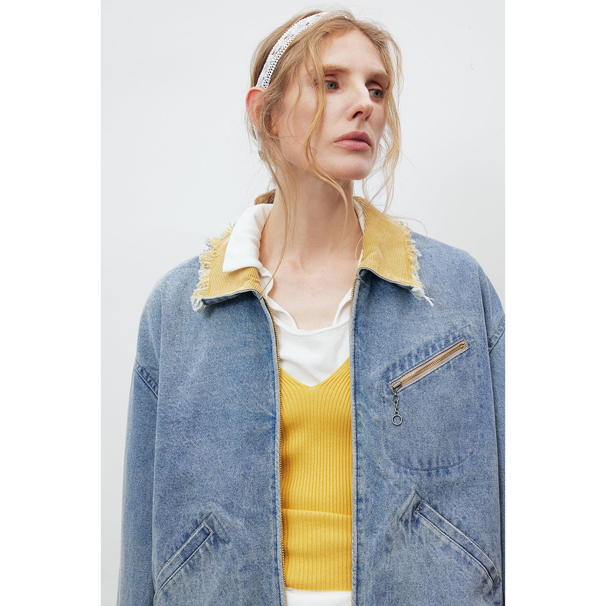 Close view of a model wearing a light blue denim jacket with a frayed yellow collar and zippered chest pocket.